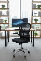 Modern office chair in front of a desk with a computer setup, in a room with large windows and bookshelves.
