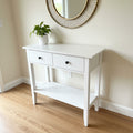 White console table with two drawers and a shelf in a store setting.