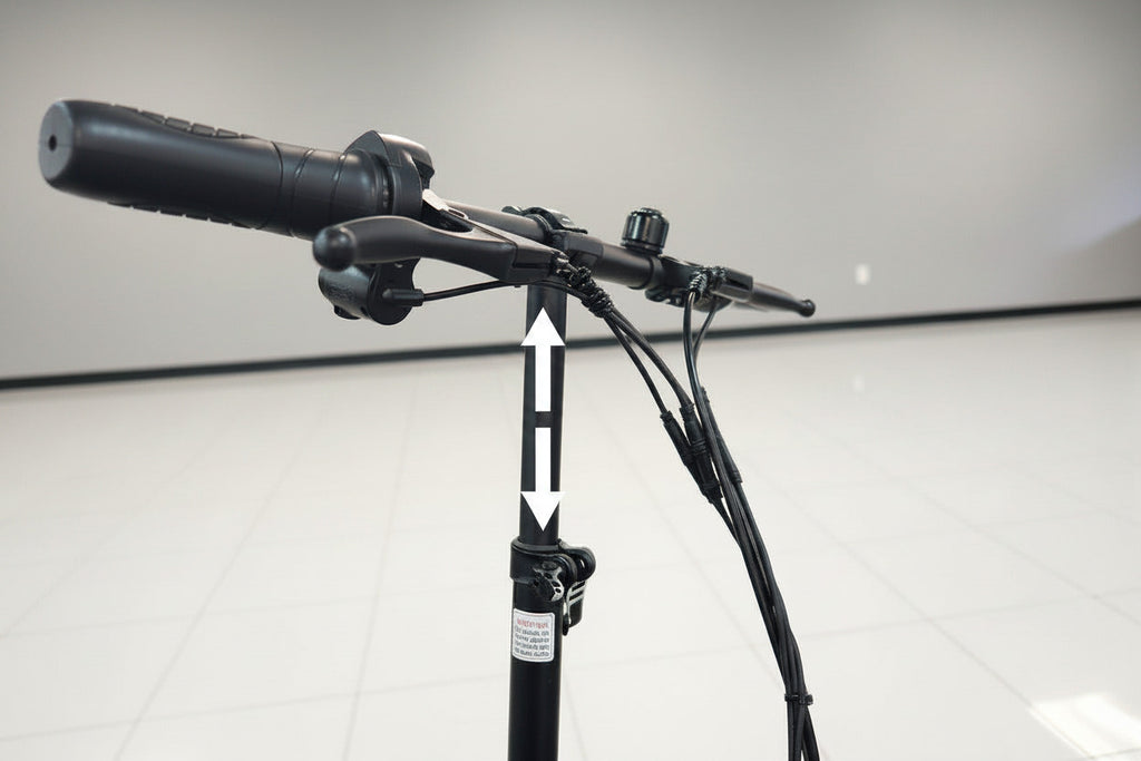 Close-up of a black electric scooter handlebar assembly with a textured grip, brake levers, and wiring on a white tiled indoor floor against a light gray wall.