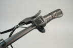 Close-up of a black electric bicycle handlebar with a digital throttle control display, showing the throttle grip and brake lever in a workshop setting.