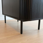 A close-up of a dark wood mid-century modern cabinet or sideboard with vertical slats, supported by four tapered legs, set on a textured gray carpet.