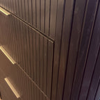 Close-up of a dark brown wooden cabinet or dresser with vertical ribbed drawer fronts and small rectangular metal pulls, photographed indoors.