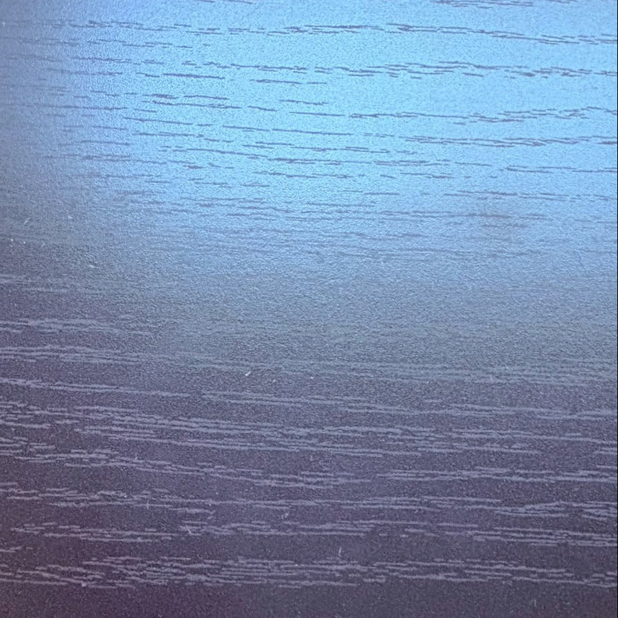 A close-up of a dark wood grain surface, likely a table top, with a blue reflective sheen and a person's shoes visible at the bottom edge.