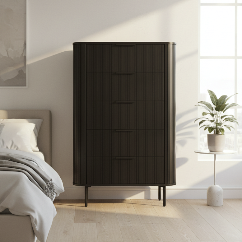 A tall black ribbed dresser or chest with five drawers stands in a modern, sunlit bedroom next to a bed and a small potted plant.