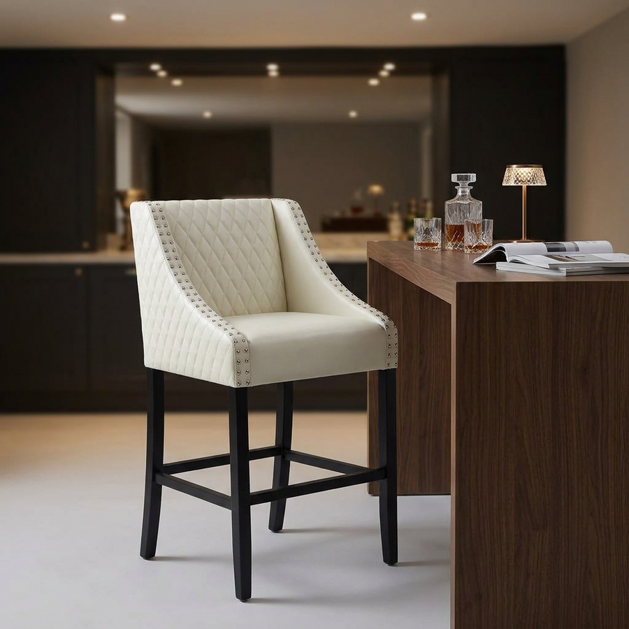 Cream tufted faux leather bar stool with nailhead trim beside a walnut home bar